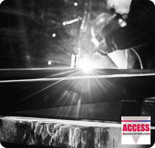 A black and white image of a close up of someone welding a door frame with a hand welder. The Access Door Systems logo is in the bottom right, mainly just text.