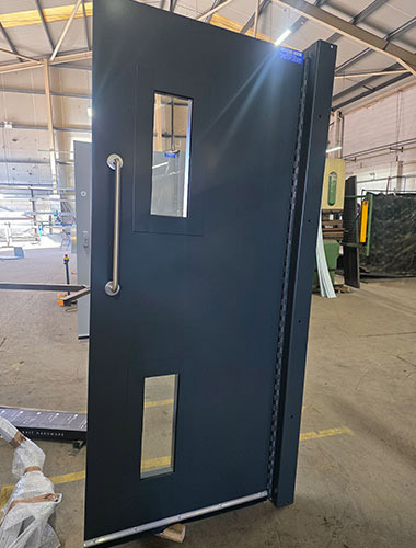 A large, dark grey, industrial metal door and frame, propped up in a workshop.